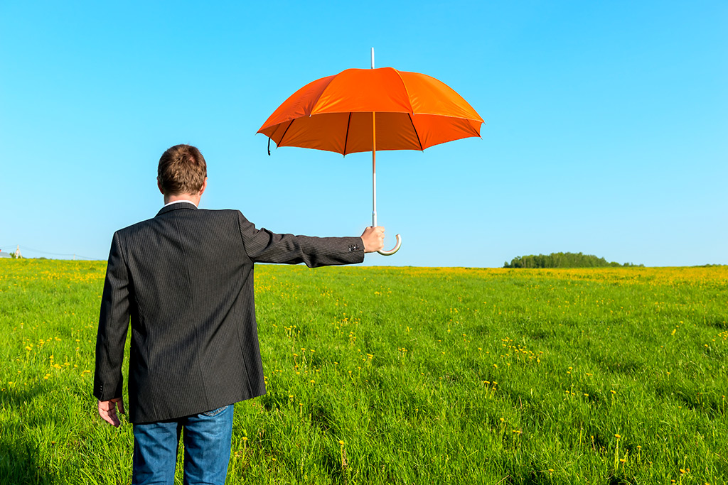 Sous un temps ensoleillé, un homme en veste noir et en jean en face d'une prairie tenant dans sa main droite un parapluie orange ouvert