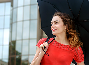 Une femme en robe rouge est sous un parapluie noir sur un fond d’immeubles de bureaux